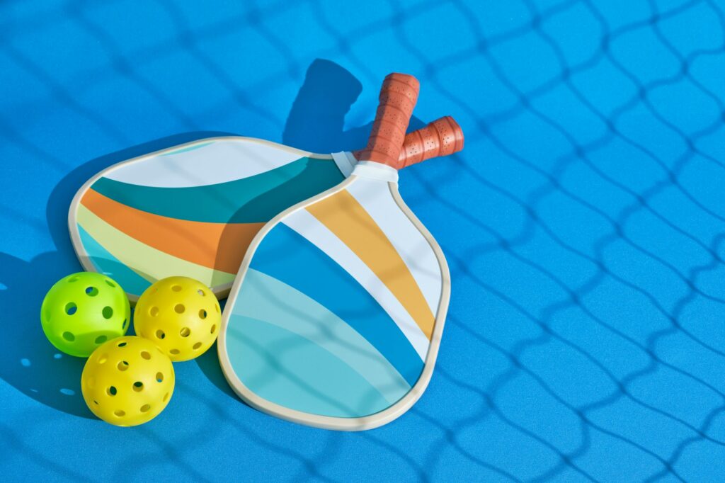 two pickleball paddles with some balls next to them with the shadow of a net in front